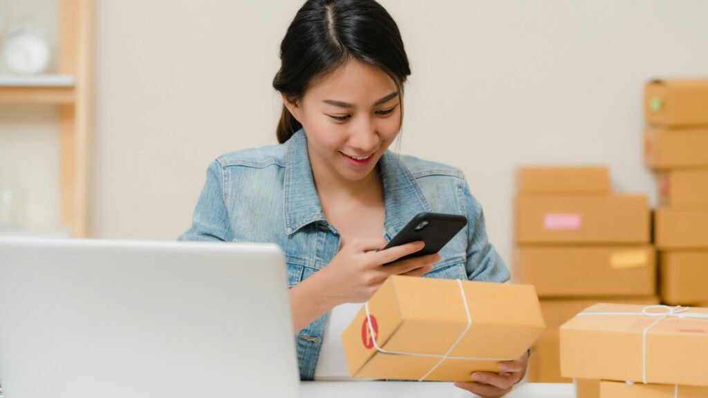 Dueña de pequeña tienda online preparando pedidos junto a su portátil