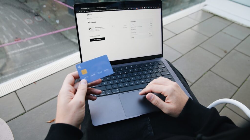Persona frente a un portátil con una tienda online abierta y una tarjeta bancaria en la mano