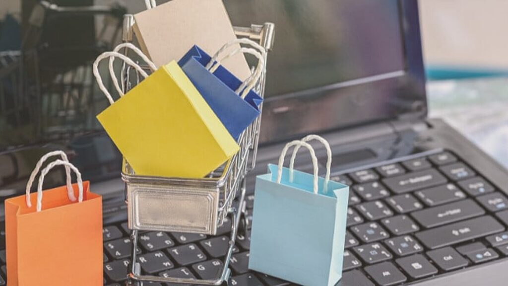 Bolsas de la compra en miniatura dentro de un carrito sobre el teclado de un portátil