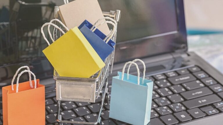 Bolsas de la compra en miniatura dentro de un carrito sobre el teclado de un portátil