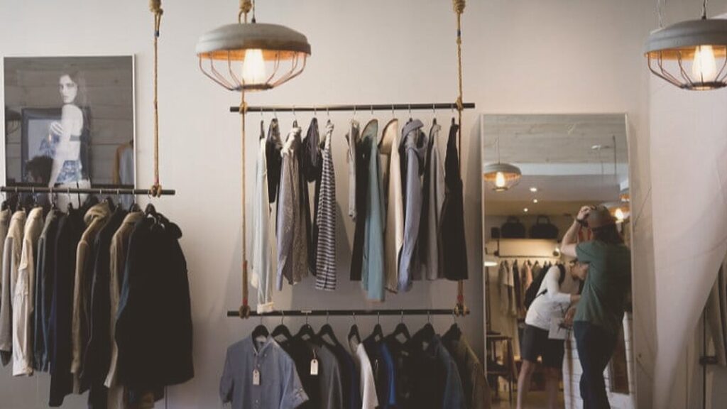 Interior de una tienda de ropa con un perchero y clientes al fondo