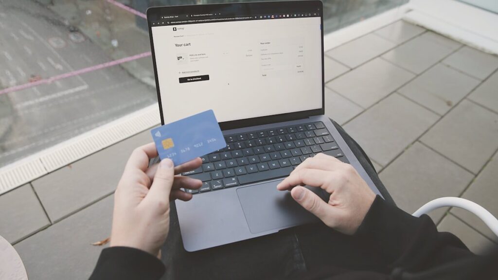 Persona frente a un portátil con una tienda online abierta y una tarjeta bancaria en la mano