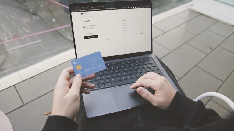 Persona frente a un portátil con una tienda online abierta y una tarjeta bancaria en la mano