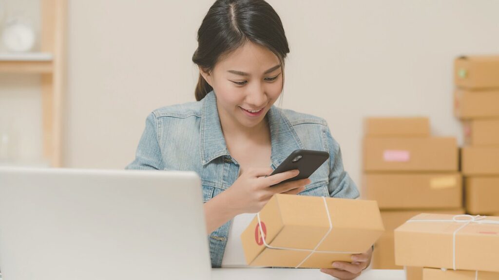 Dueña de pequeña tienda online preparando pedidos junto a su portátil