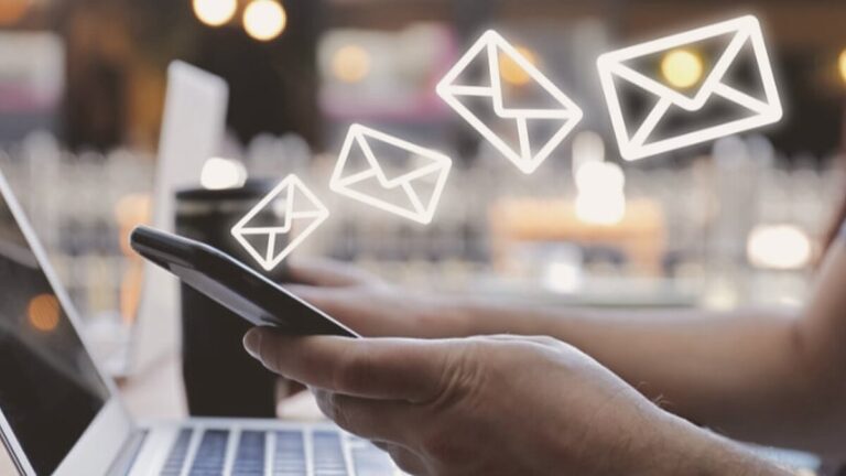 Mano sosteniendo un móvil del que salen iconos de correo, junto a un portátil